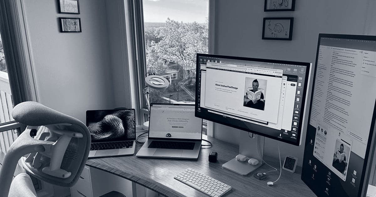 A freelance web designer's desk: Josh Miller's large monitor and two laptops by a window in Arvada, Colorado, with website work on the screens