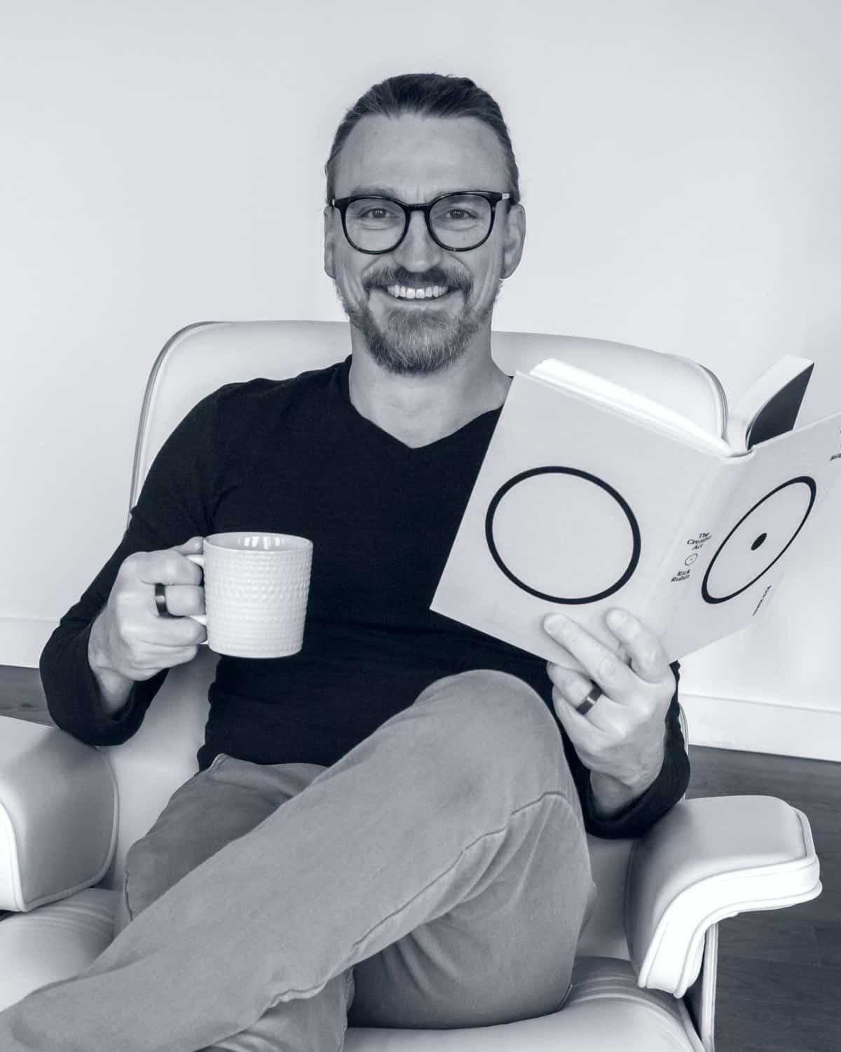 Josh Miller, freelance web designer, smiling in a lounge chair with a coffee and a book