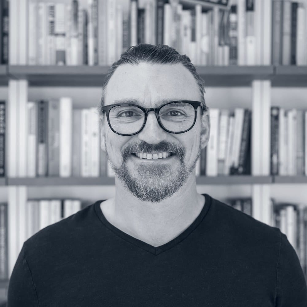 Josh Miller, freelance web designer, smiling in front of his bookshelf
