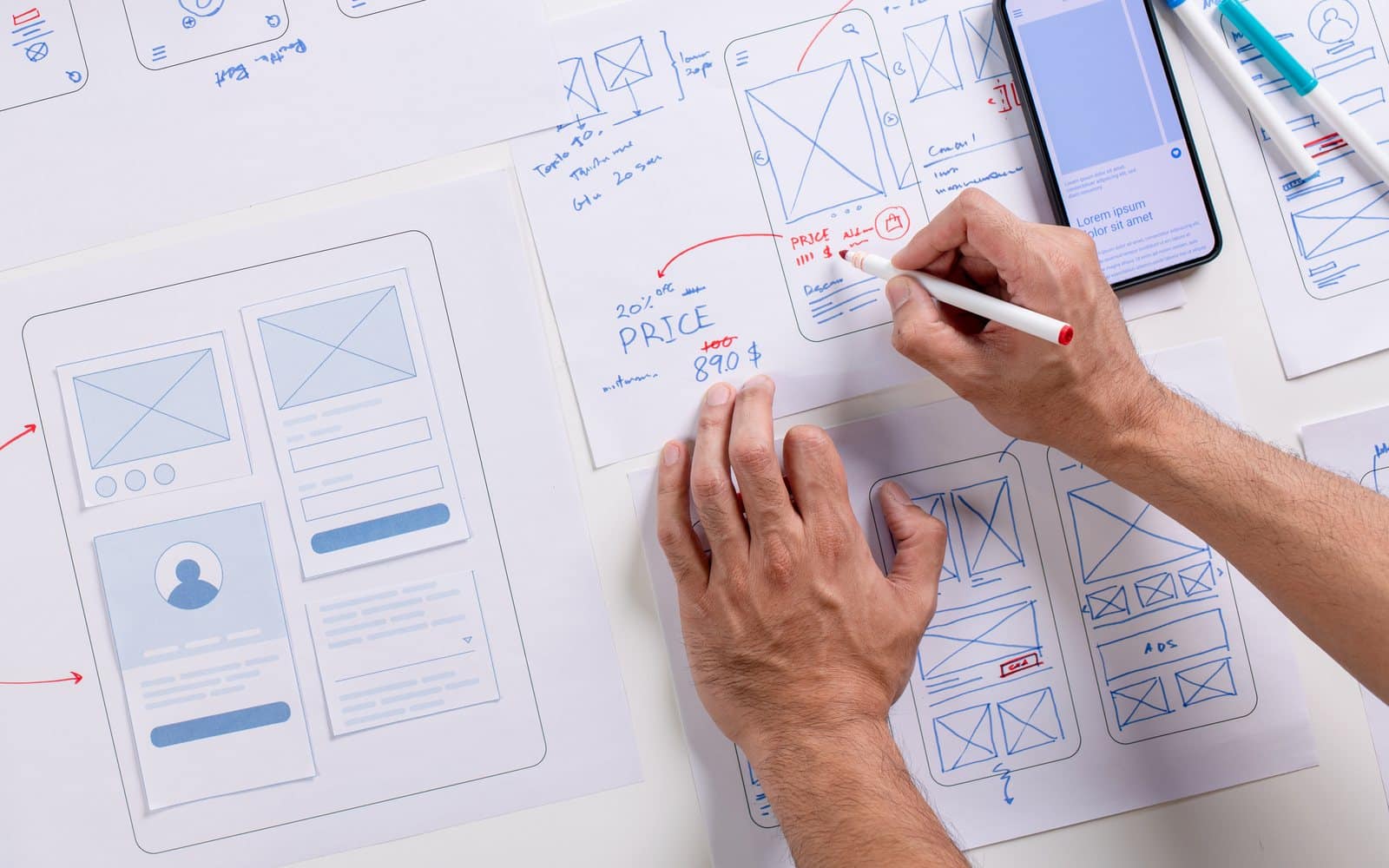 Website redesign planning: hands marking up website wireframes on paper beside a phone